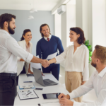 Two persons shaking hands in a meeting among other people.