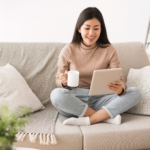 A person sitting on a couch with a tablet in one hand and a mug in the other.