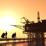 An oil rig with three persons pushing oil barrels from it
