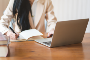 A person in front of a laptop writing in a notebook.