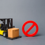 A forklift carrying a cargo box next to a ban sign